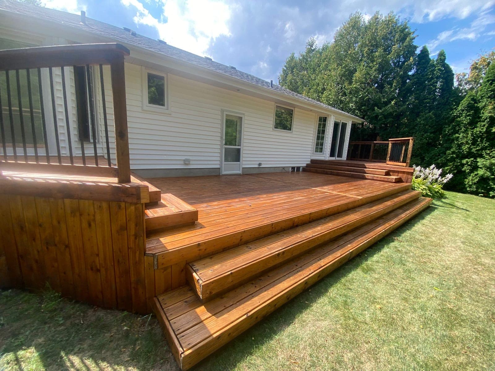 Wide deck with stairs stained cedar beside a white house
