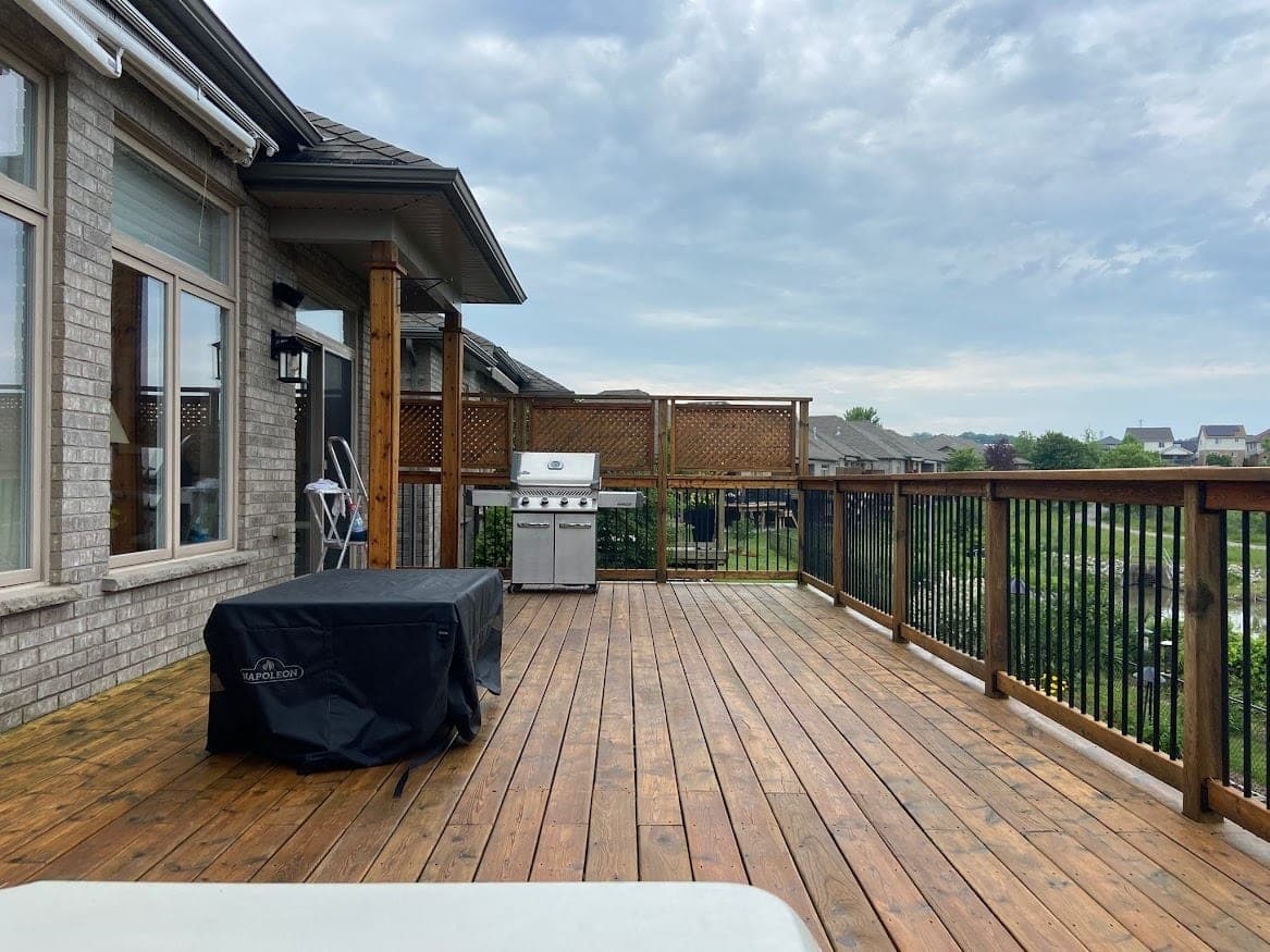 Wide stained deck with grill behind a brick home